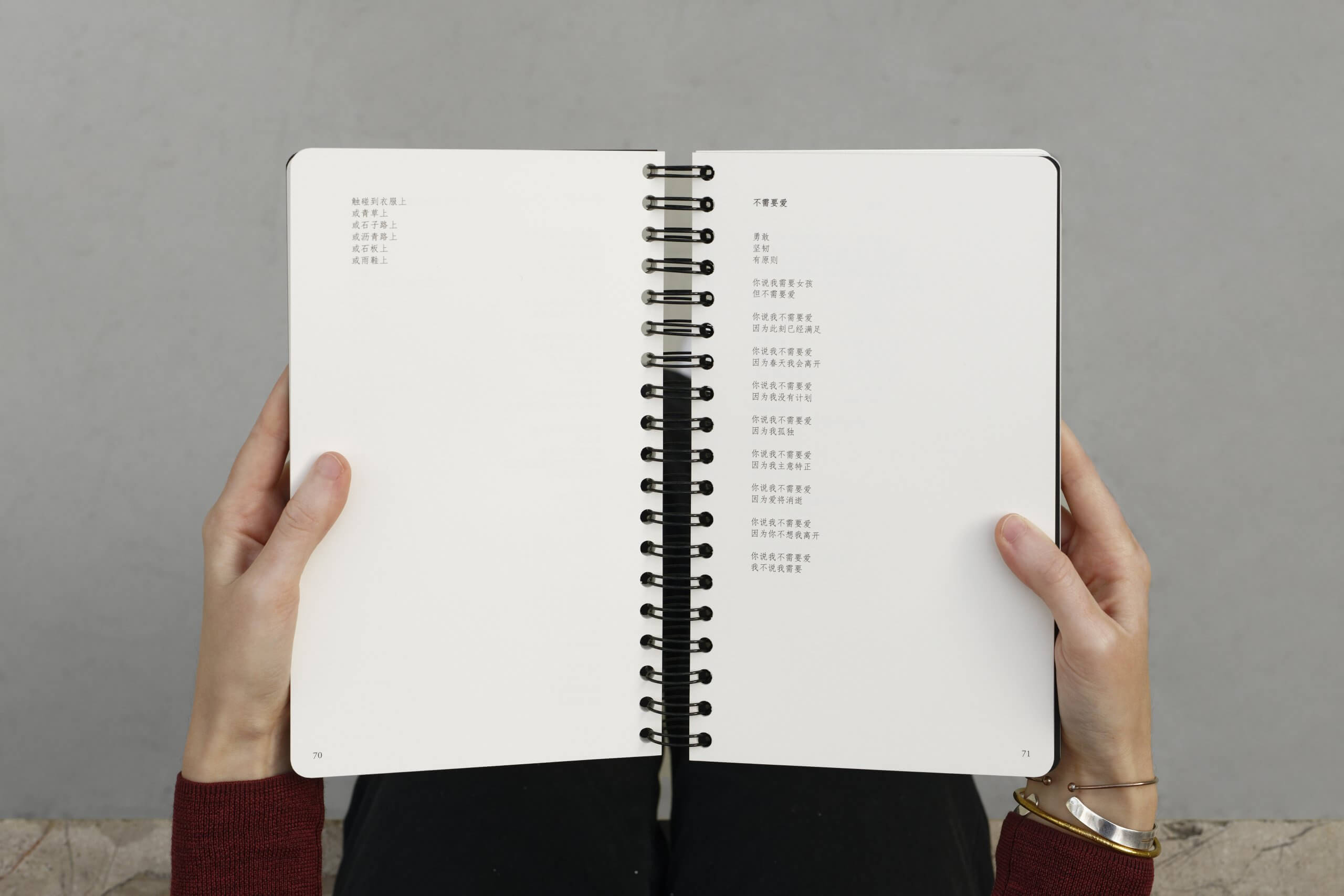 Une personne tient ouvert un cahier à spirales dont les pages contiennent du texte imprimé en chinois. La page de gauche présente une courte liste, tandis que la page de droite présente une colonne de texte plus longue. Le fond est gris uni.