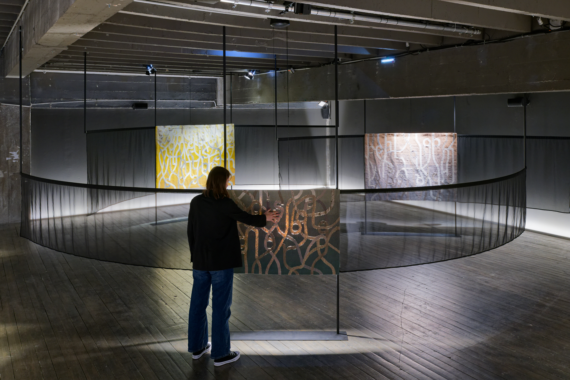 vue de l'exposition et des trois tapisseries. Un personne touche celle du premier rang