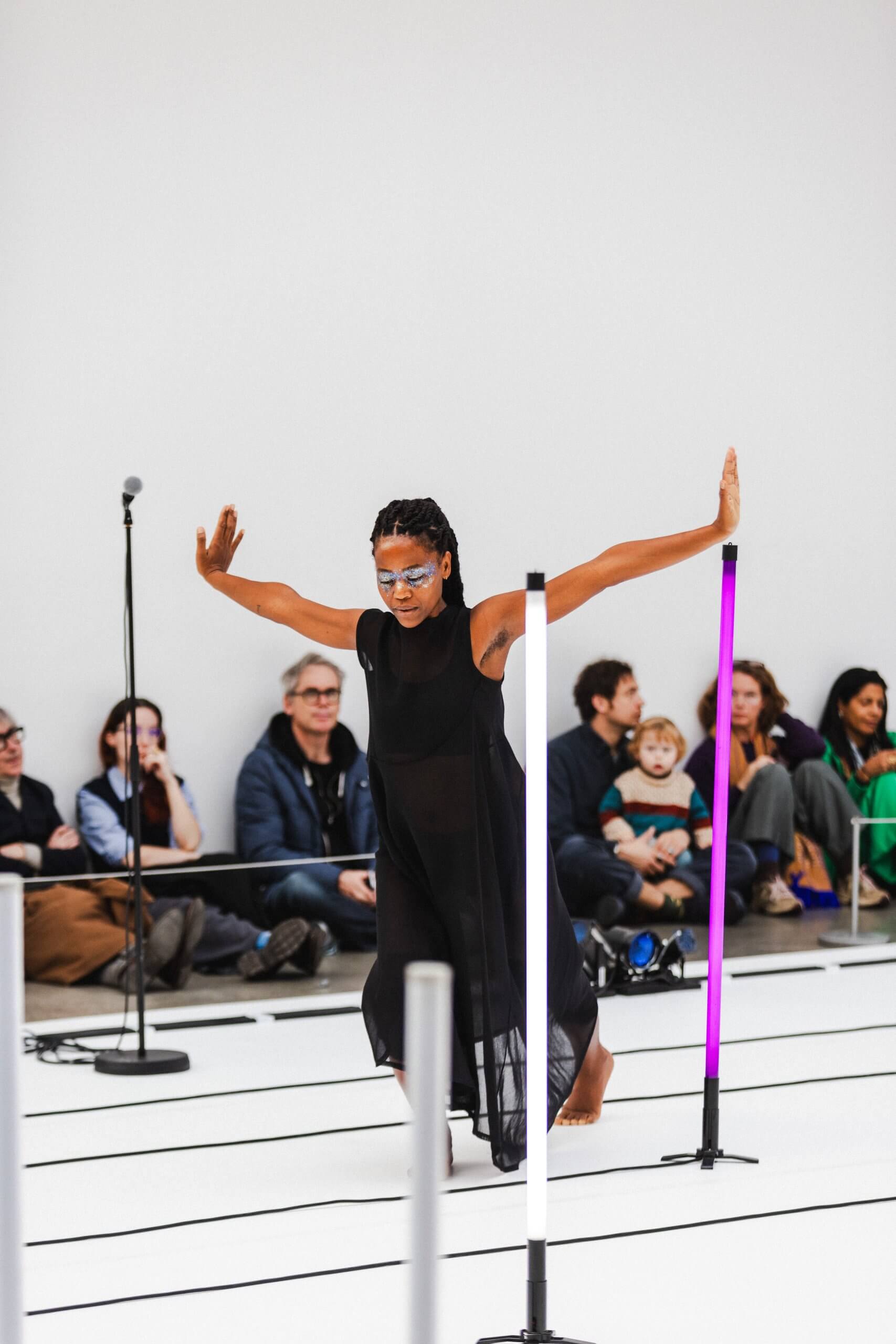 Une femme en robe noire se produit sur scène entourée de néons.