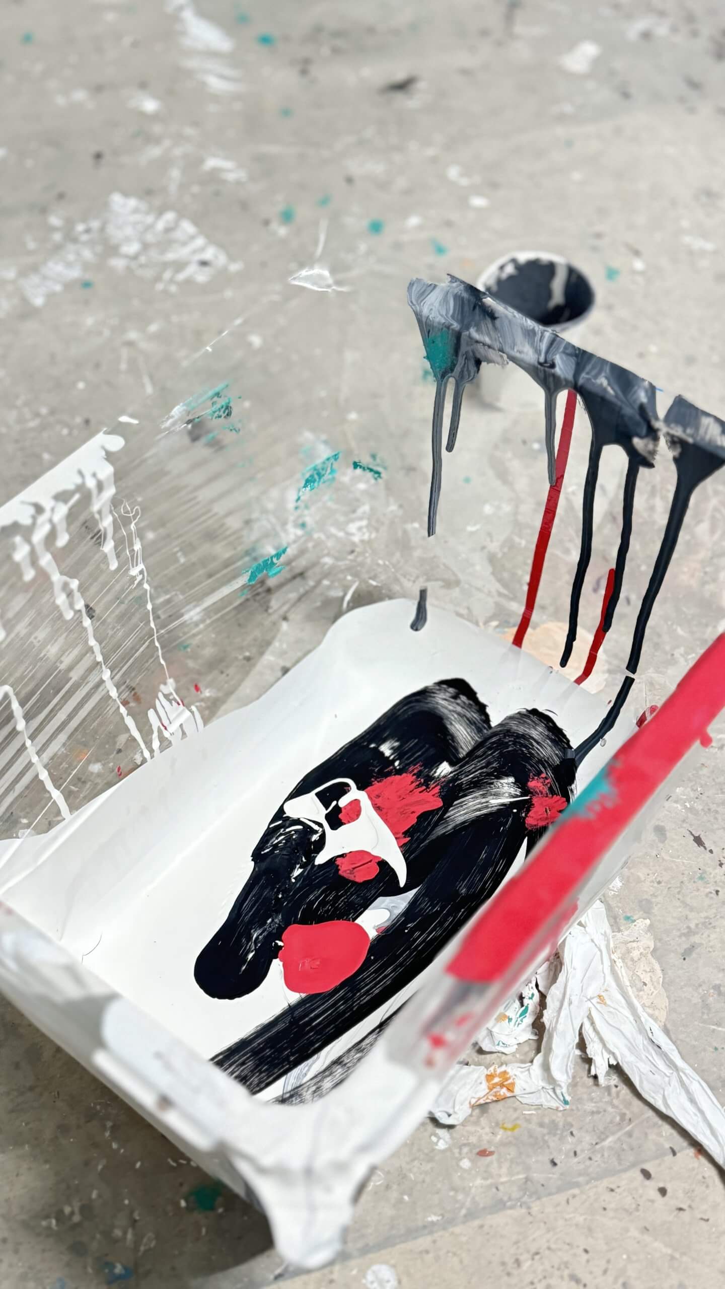 Paint tray with black, red, and white splatters, on a stained floor.