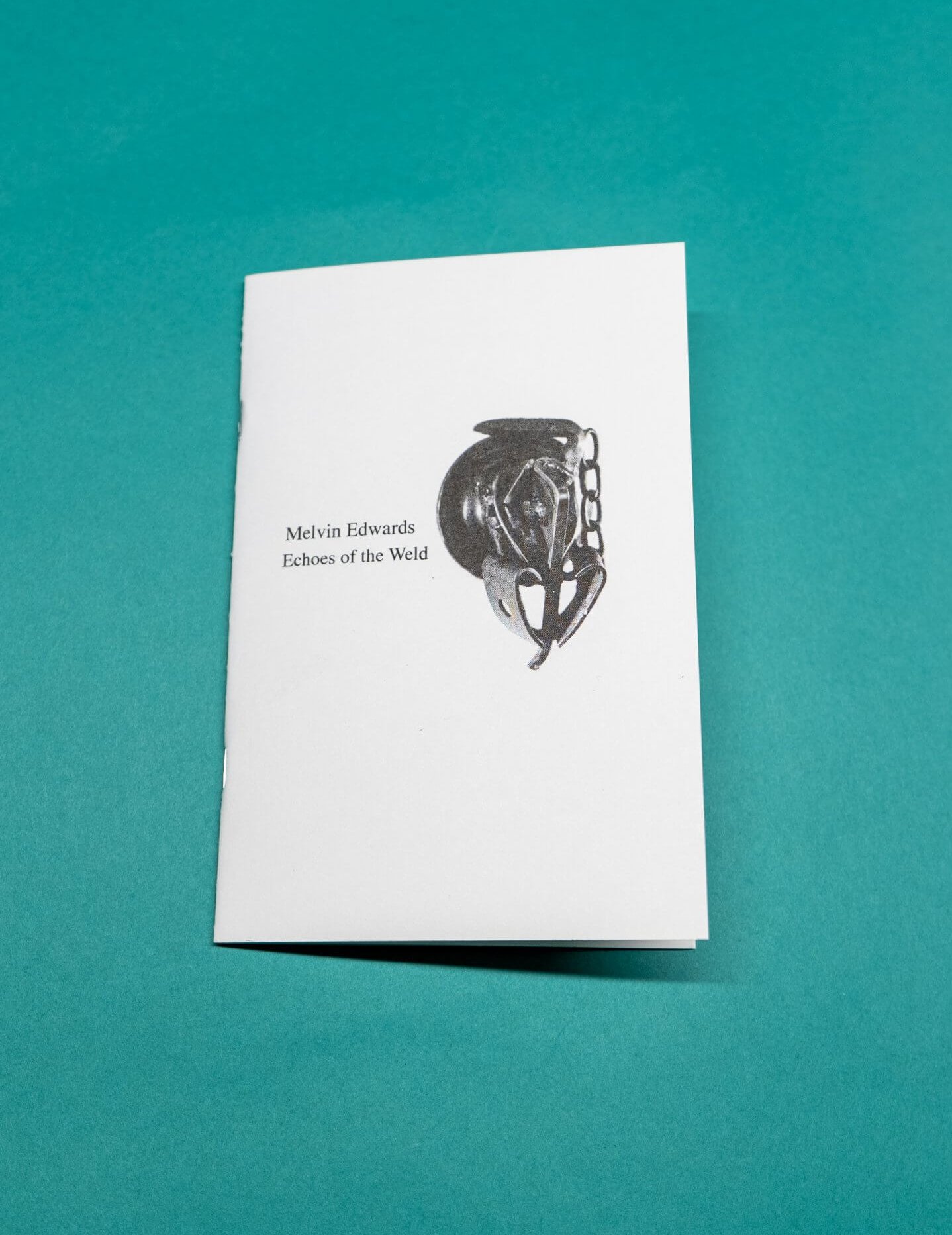 Un livret blanc intitulé Melvin Edwards Echoes of the Weld avec une illustration abstraite noire sur la couverture, placée sur un fond sarcelle.