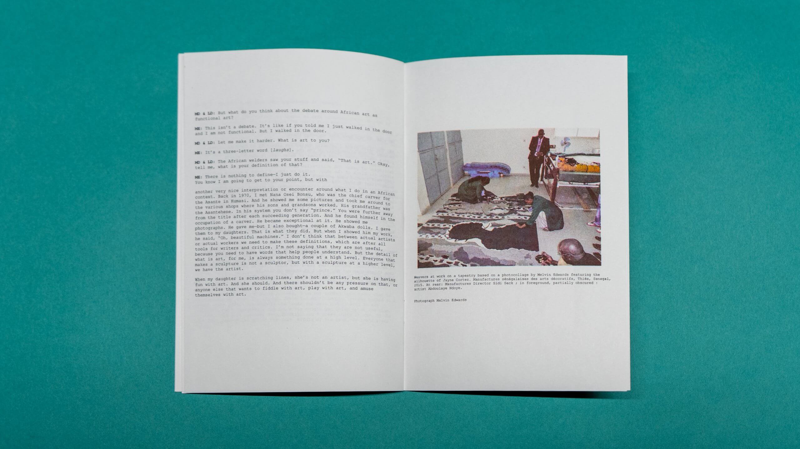 An open booklet on a teal surface displays text on the left page and a photo with people and a patterned rug on the right page.
