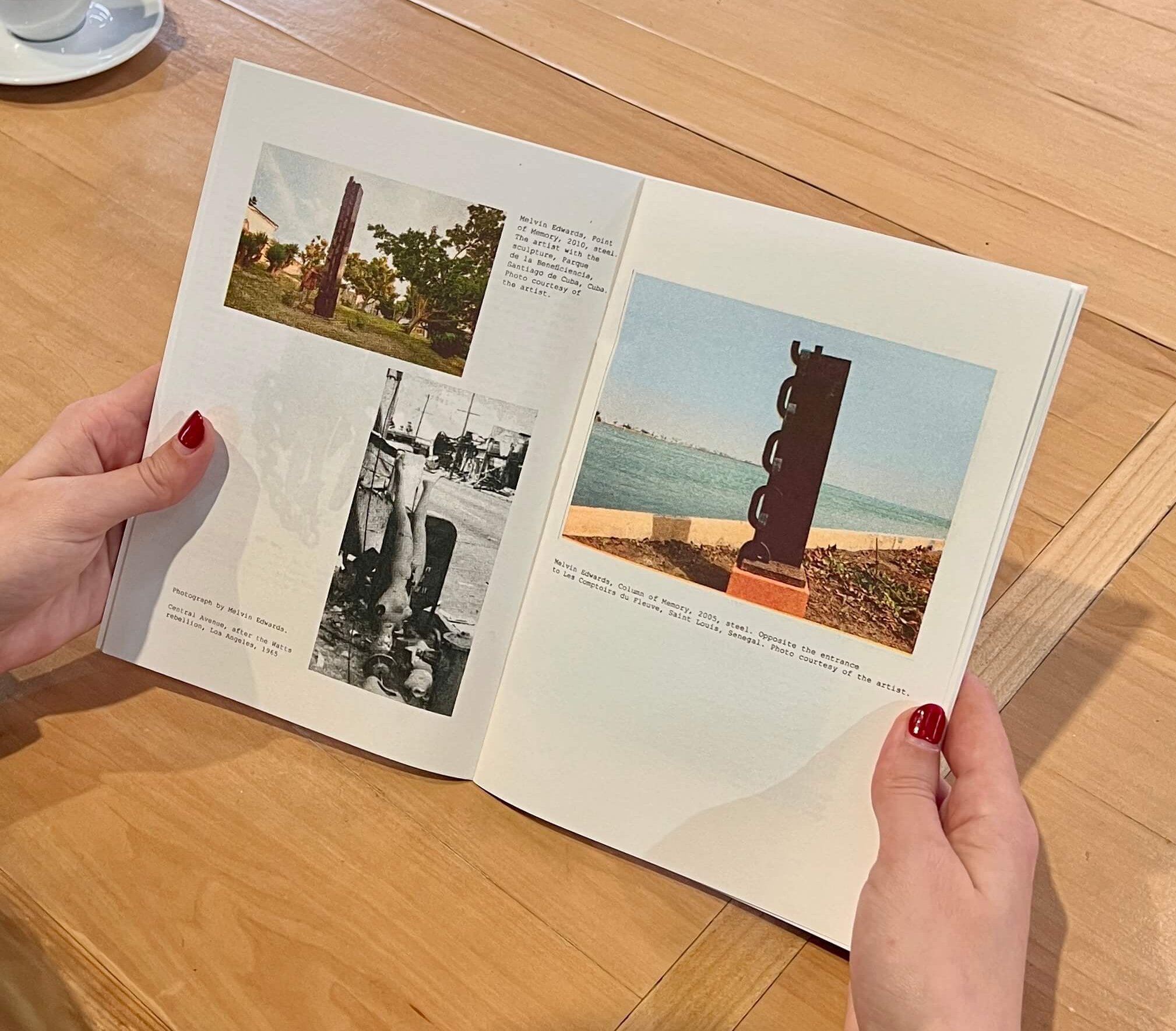 Person holding open a book showing vintage photographs and captions, with a cup of coffee on a wooden table in the background.