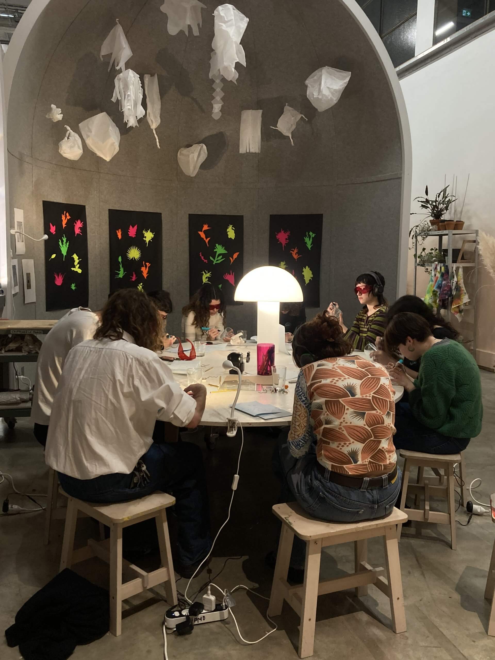 Un groupe de personnes est assis autour d'une table et travaille à l'artisanat sous un dôme, avec des décorations en papier suspendues au-dessus et des œuvres d'art colorées affichées sur les murs.