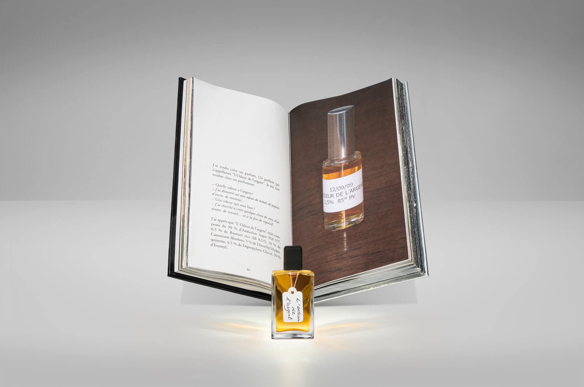 Un flacon de parfum est placé devant un livre ouvert, qui affiche une photo du même flacon sur une page et un texte sur l'autre.
