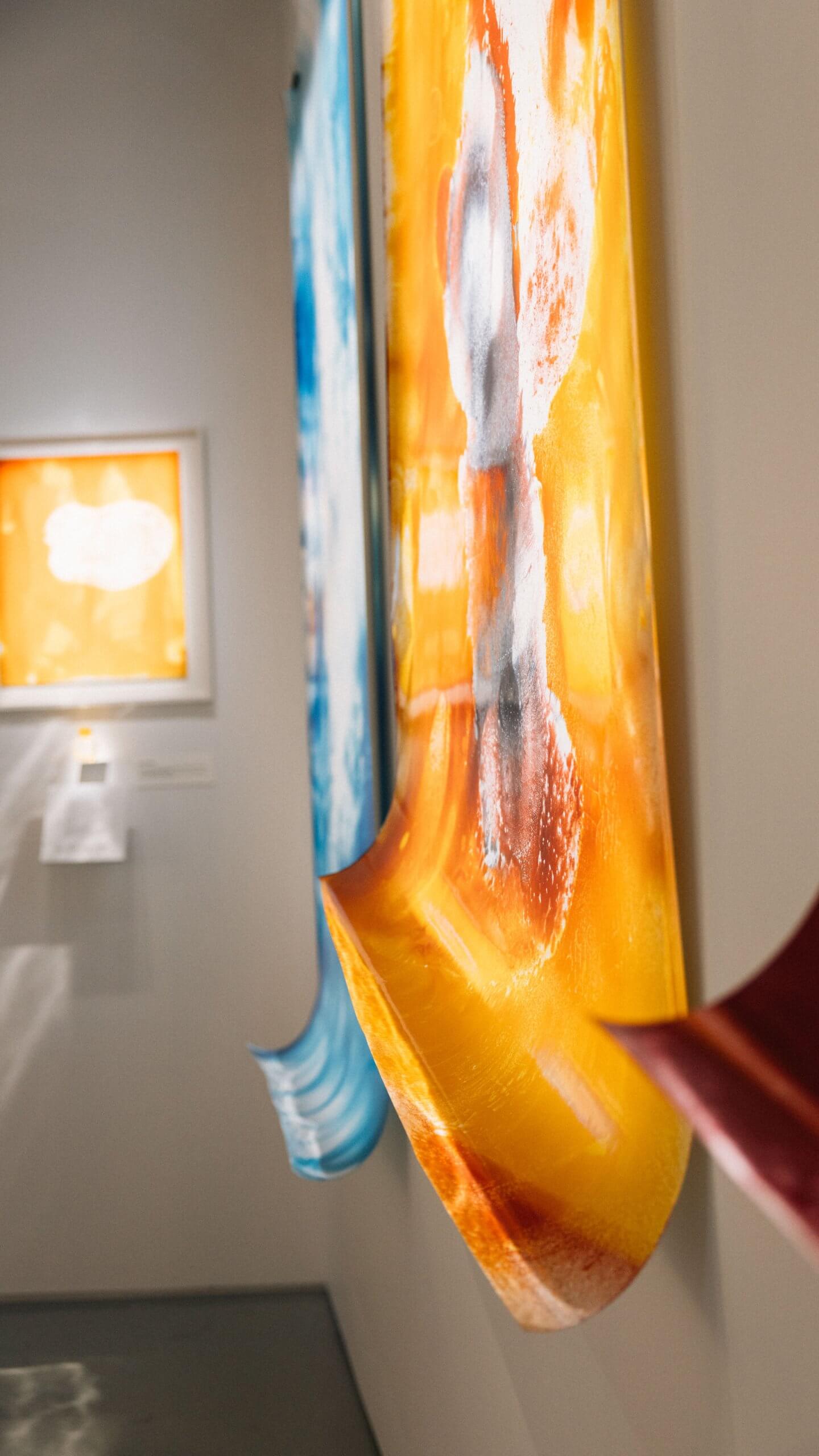 Gros plan sur des œuvres d'art murales abstraites et colorées, aux bords incurvés, exposées dans une galerie.