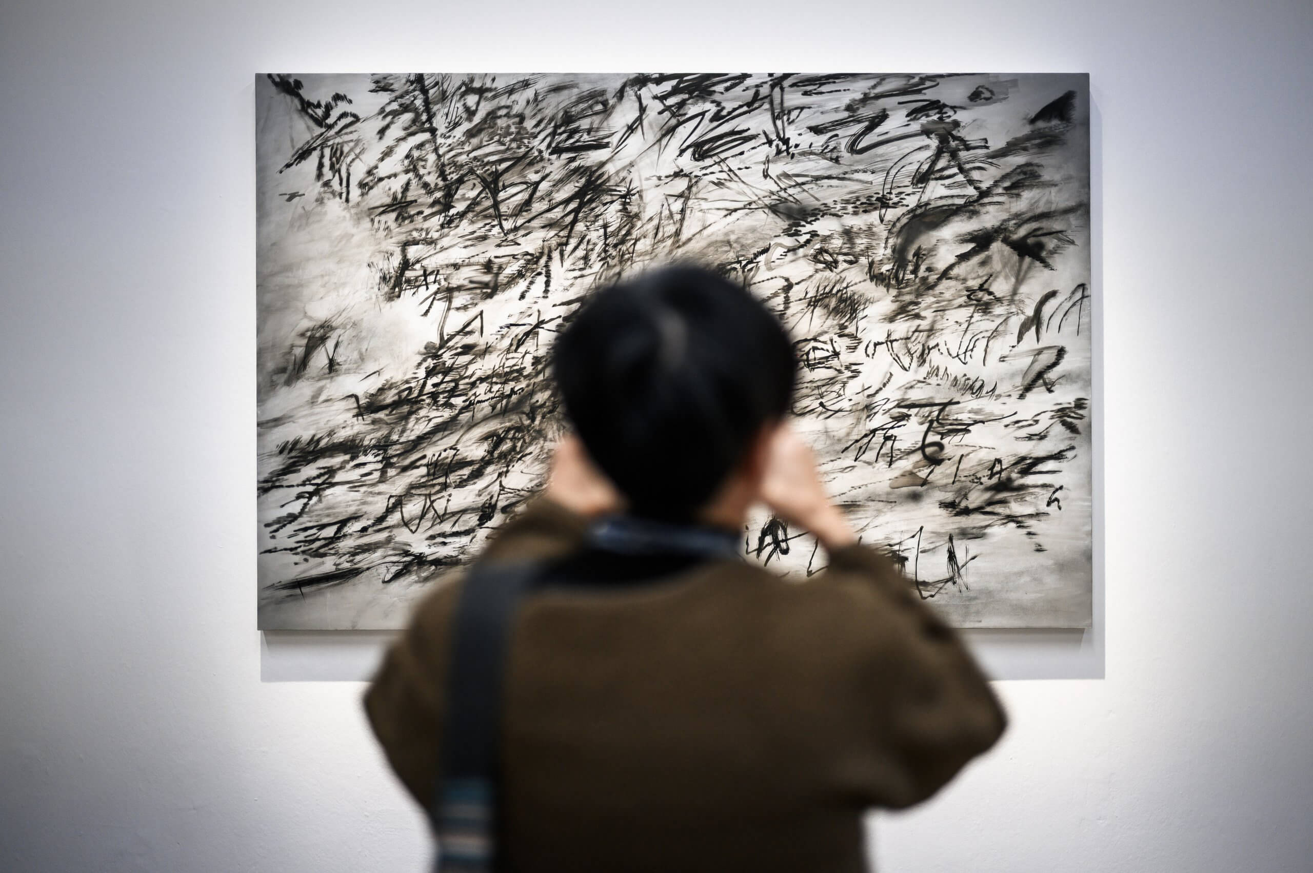 Une personne observe attentivement une œuvre d'art abstraite en noir et blanc présentant des coups de pinceau dynamiques et expressifs sur le mur d'une galerie.