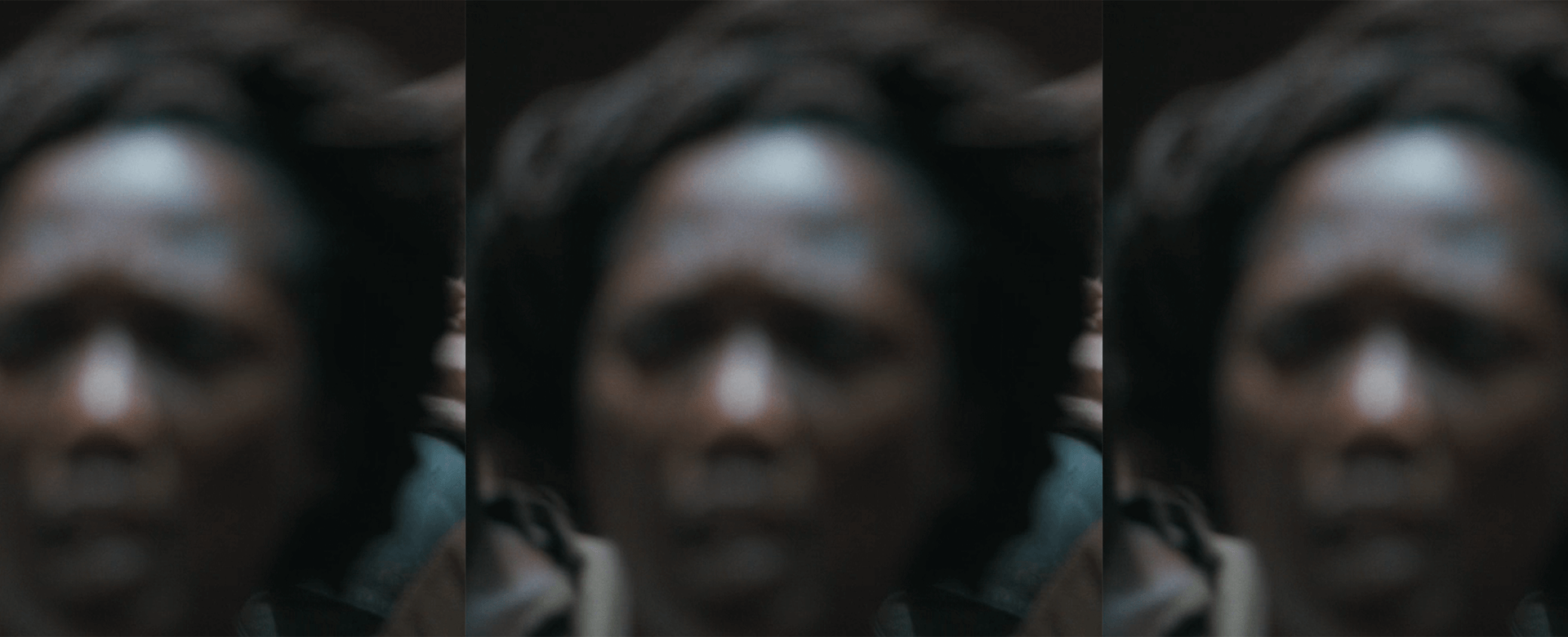 A blurry, close-up image of a persons face with indistinct features, set against a dark background.