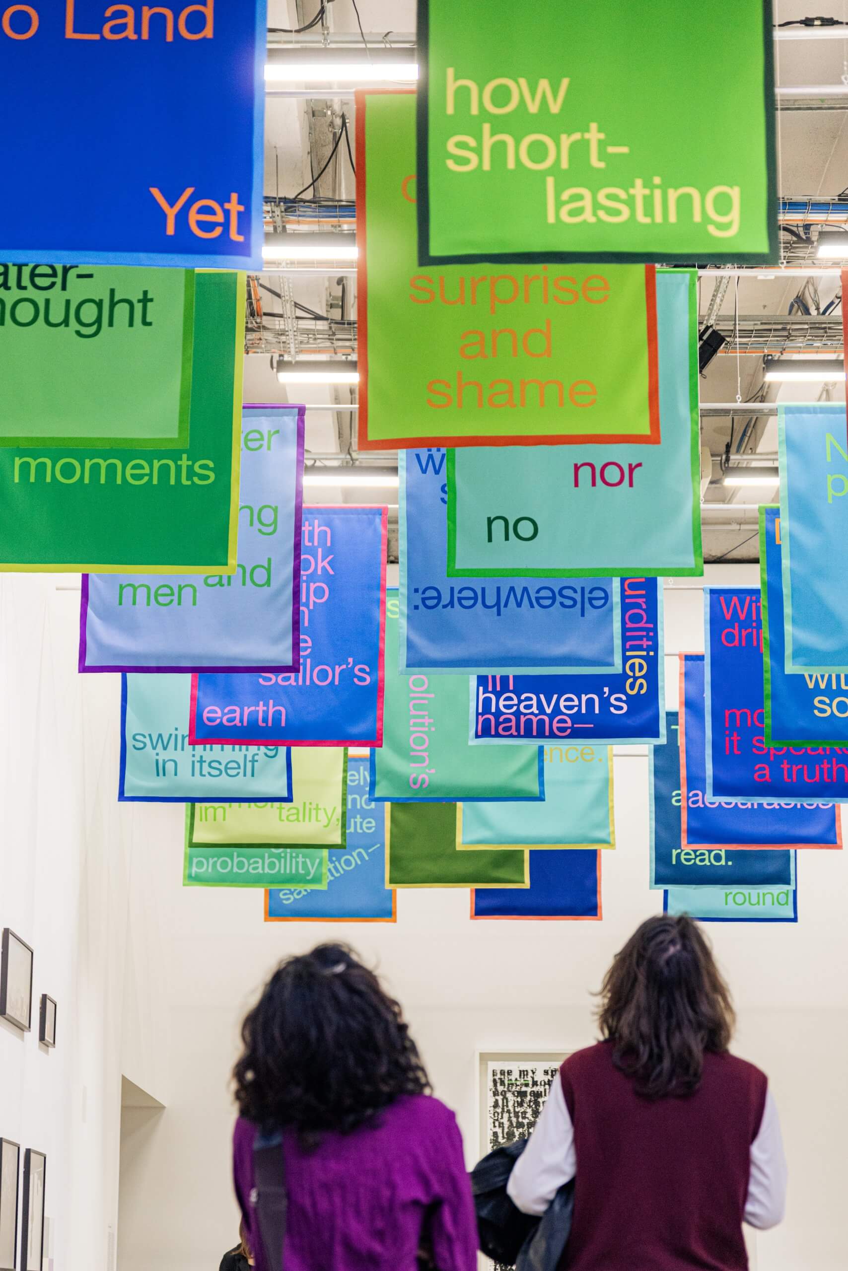 Deux personnes regardent des bannières de texte aux couleurs vives suspendues au plafond, chacune affichant des mots et des phrases différents en caractères gras.