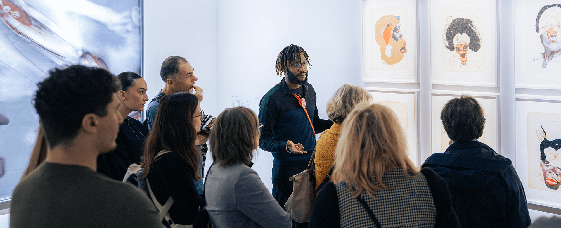 Un groupe de personnes écoute un médiateur expliquer deux œuvres de l'exposition nommée "Echo Delay Reverb" exposées sur un mur blanc.
