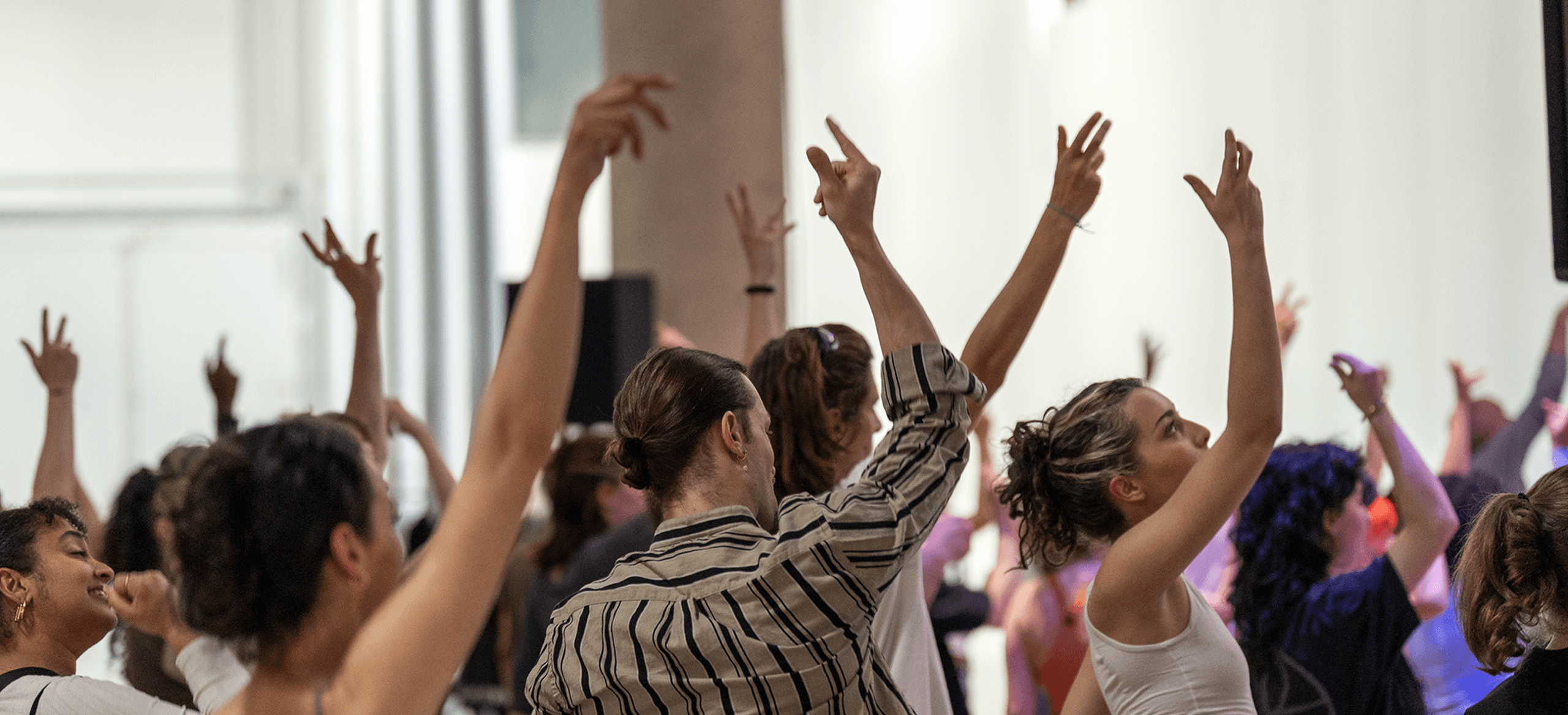 Un groupe de personnes se tient à l'intérieur, les bras levés, et participe à une activité ou à un cours de danse.