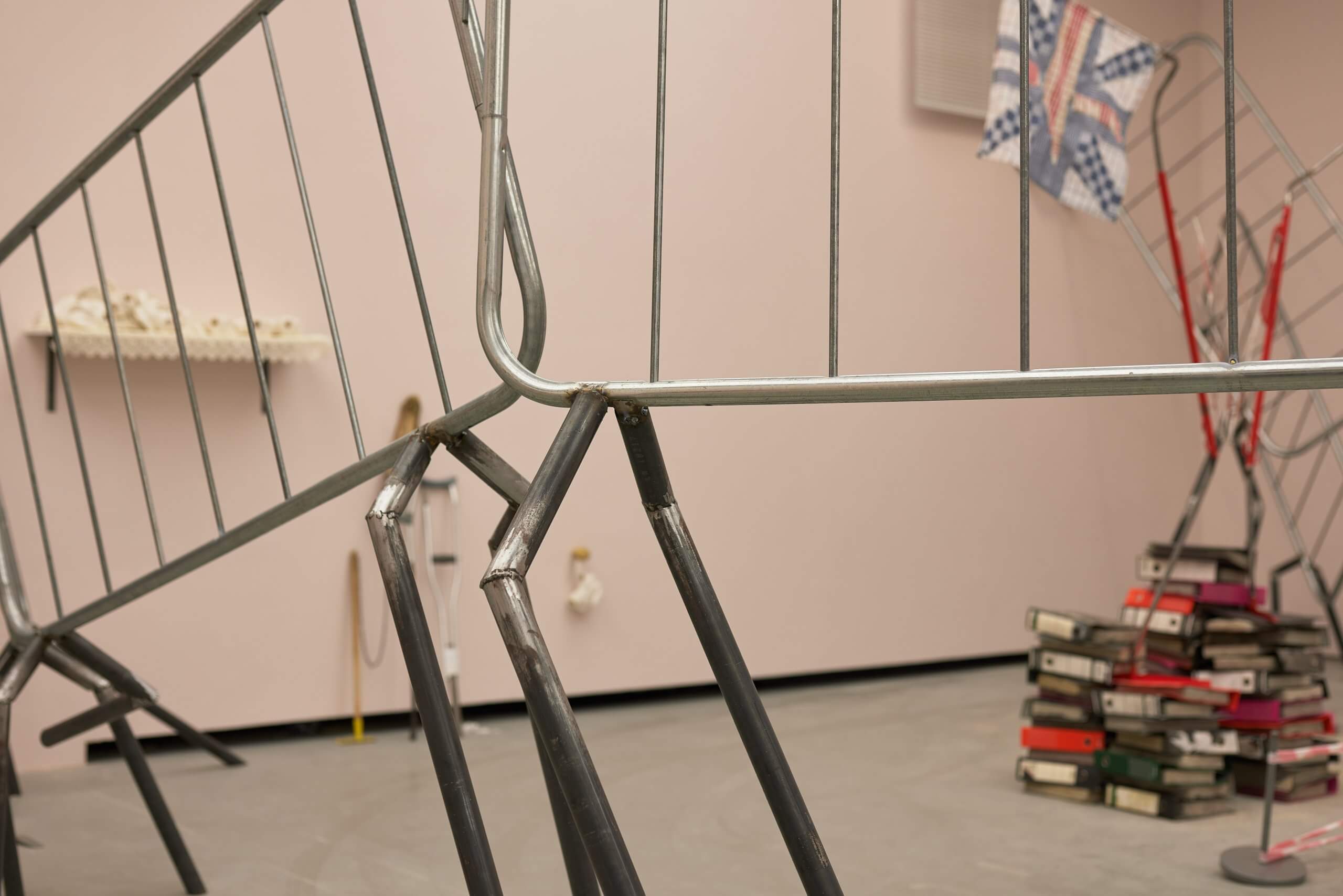 Gros plan sur des barrières métalliques pliées dans une pièce où se trouve une installation artistique, avec une pile de livres et d'autres objets à l'arrière-plan.