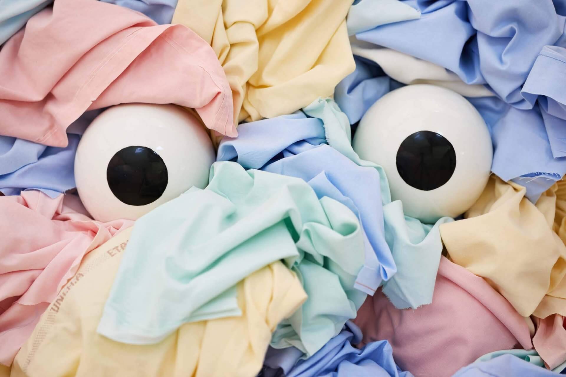 Deux grands globes oculaires artificiels sont partiellement recouverts de tissus aux couleurs pastel dans les tons rose, jaune, bleu et vert.