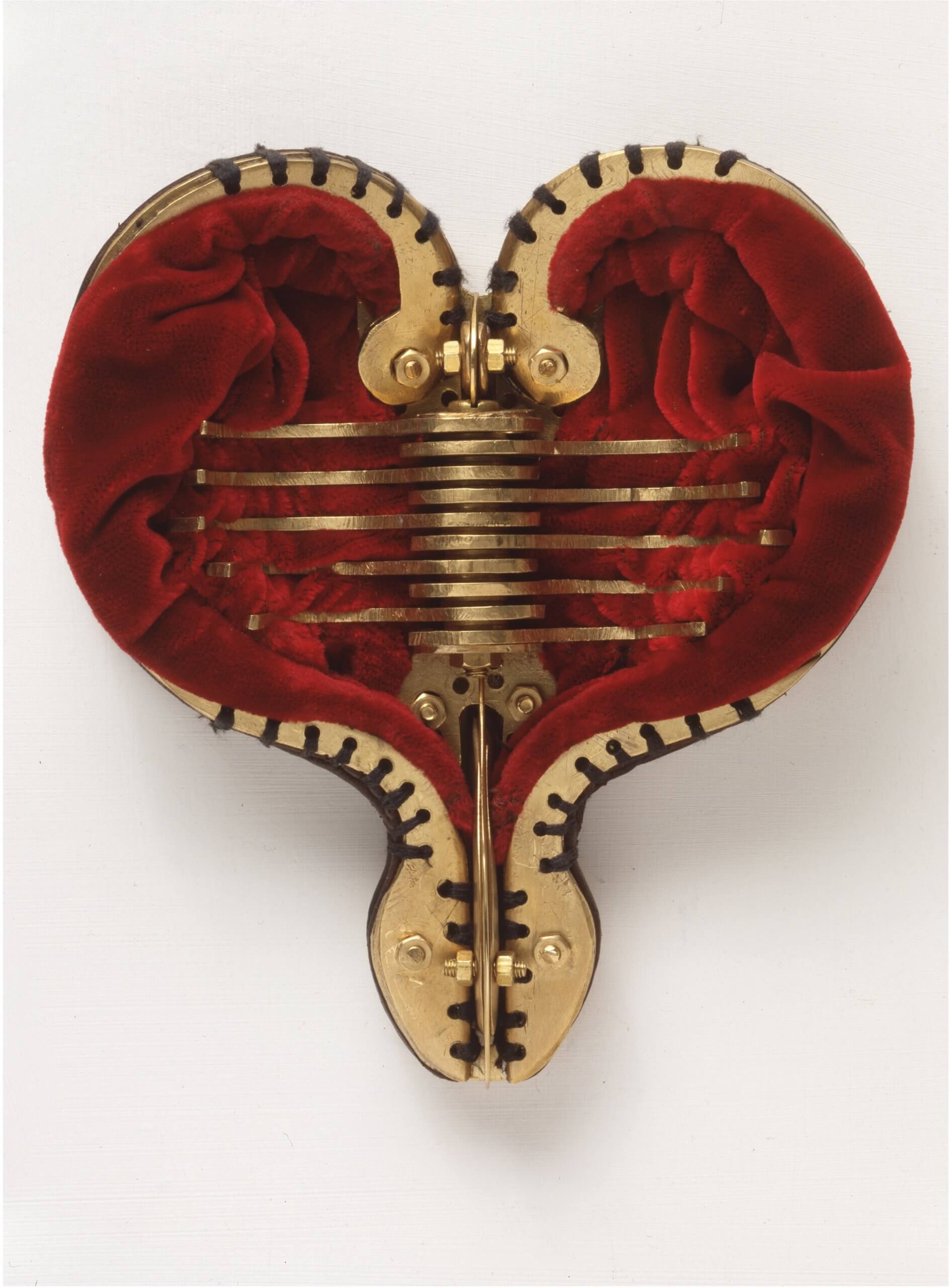 Objet en forme de cœur avec des composants mécaniques métalliques et une doublure en velours rouge, ressemblant à un cœur anatomique, présenté sur un fond blanc uni.