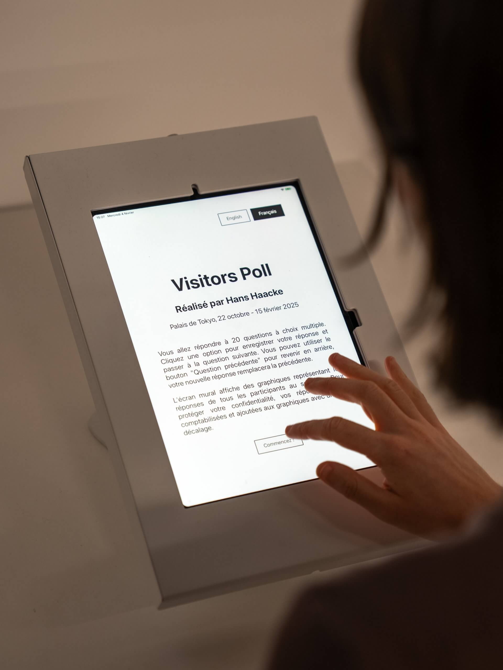 A person interacts with a touchscreen displaying a Visitors Poll survey by Hans Haacke at Palais de Tokyo, featuring information in French about the exhibit.