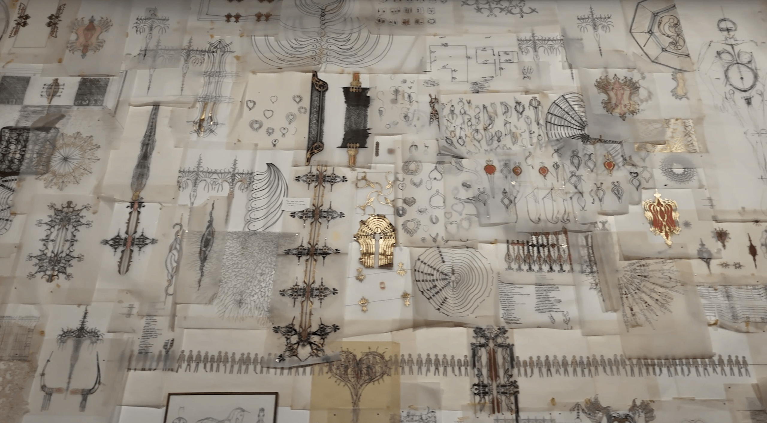 Un grand collage de croquis techniques, de diagrammes et de dessins géométriques, disposés sur un mur en couches superposées, certains comportant des accents métalliques et des motifs ornés.