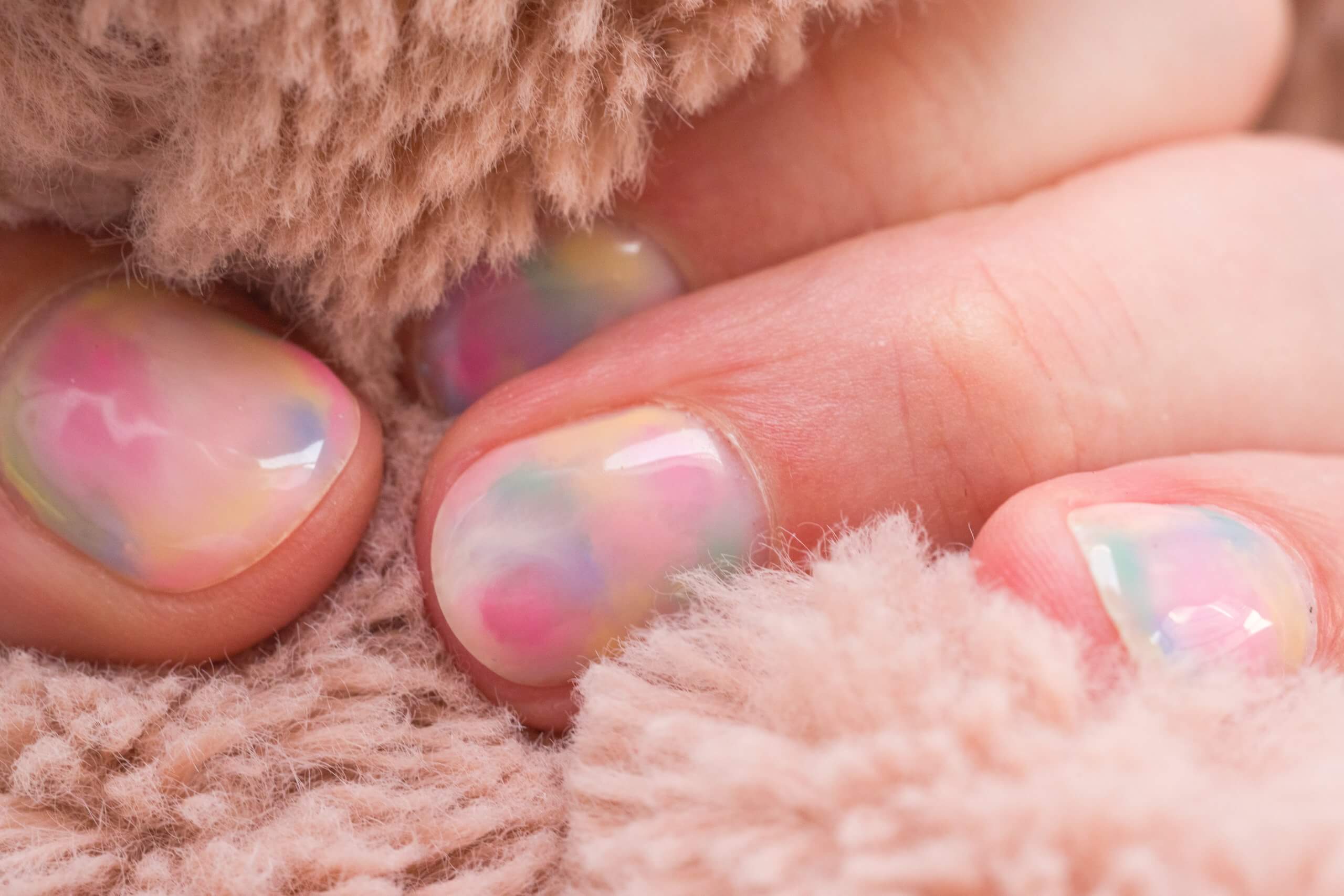 Gros plan sur des doigts ornés d'un motif de marbre pastel, entourés d'un tissu doux et moelleux de couleur beige.