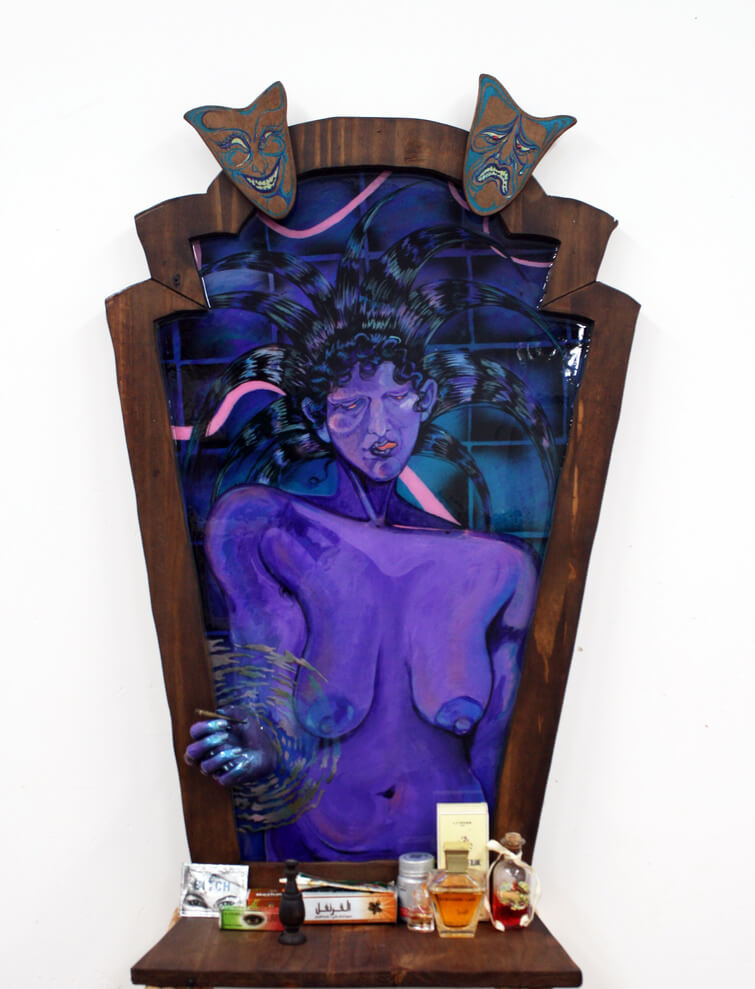 A mixed-media artwork featuring a purple female figure with flowing hair in a wooden frame, two theatrical masks on top, and various small objects on a shelf below.