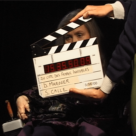 Une personne tient un panneau d'affichage devant une femme assise. Le clap affiche des détails sur le film, notamment les noms de D. Maroger et S. Calle et la date du 28 mars 2000.