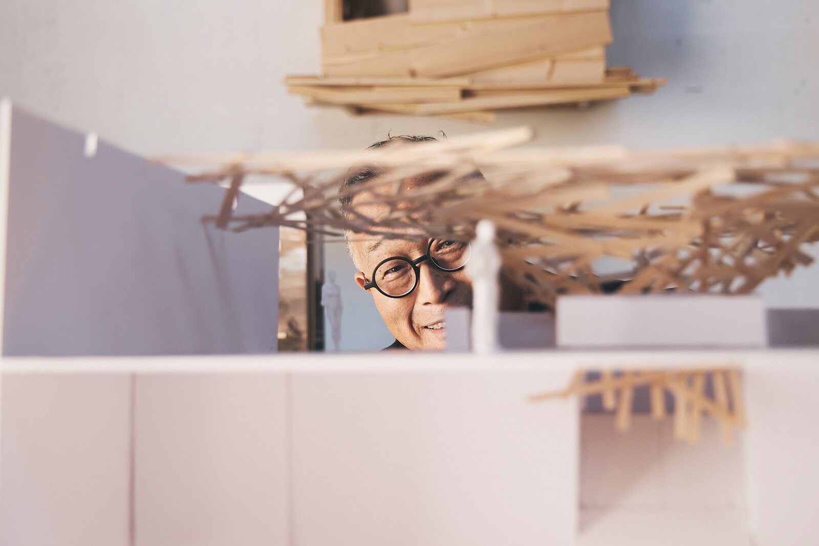 Une personne portant des lunettes regarde à travers une maquette architecturale partiellement construite en bois et en carton.