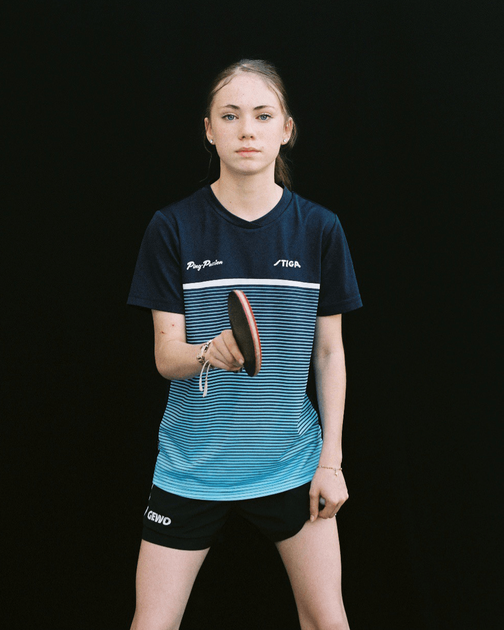 Une jeune femme en tenue de sport tient une raquette de tennis de table, sur fond noir.
