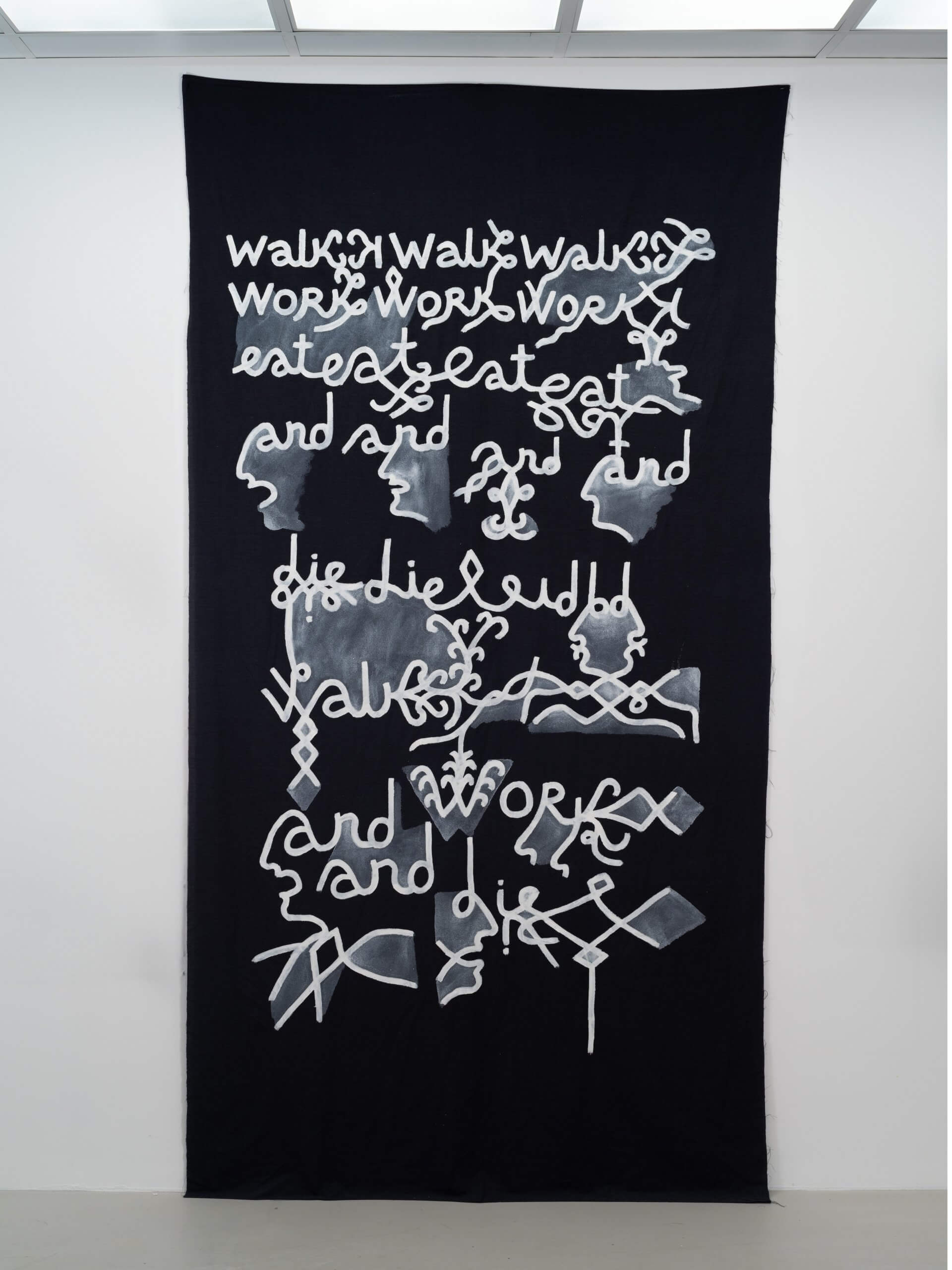 Une œuvre d'art en tissu noir avec un texte stylisé blanc disant "walk walk walk, work work work work, eat eat eat, and die", entrecoupé de visages abstraits et de formes géométriques.