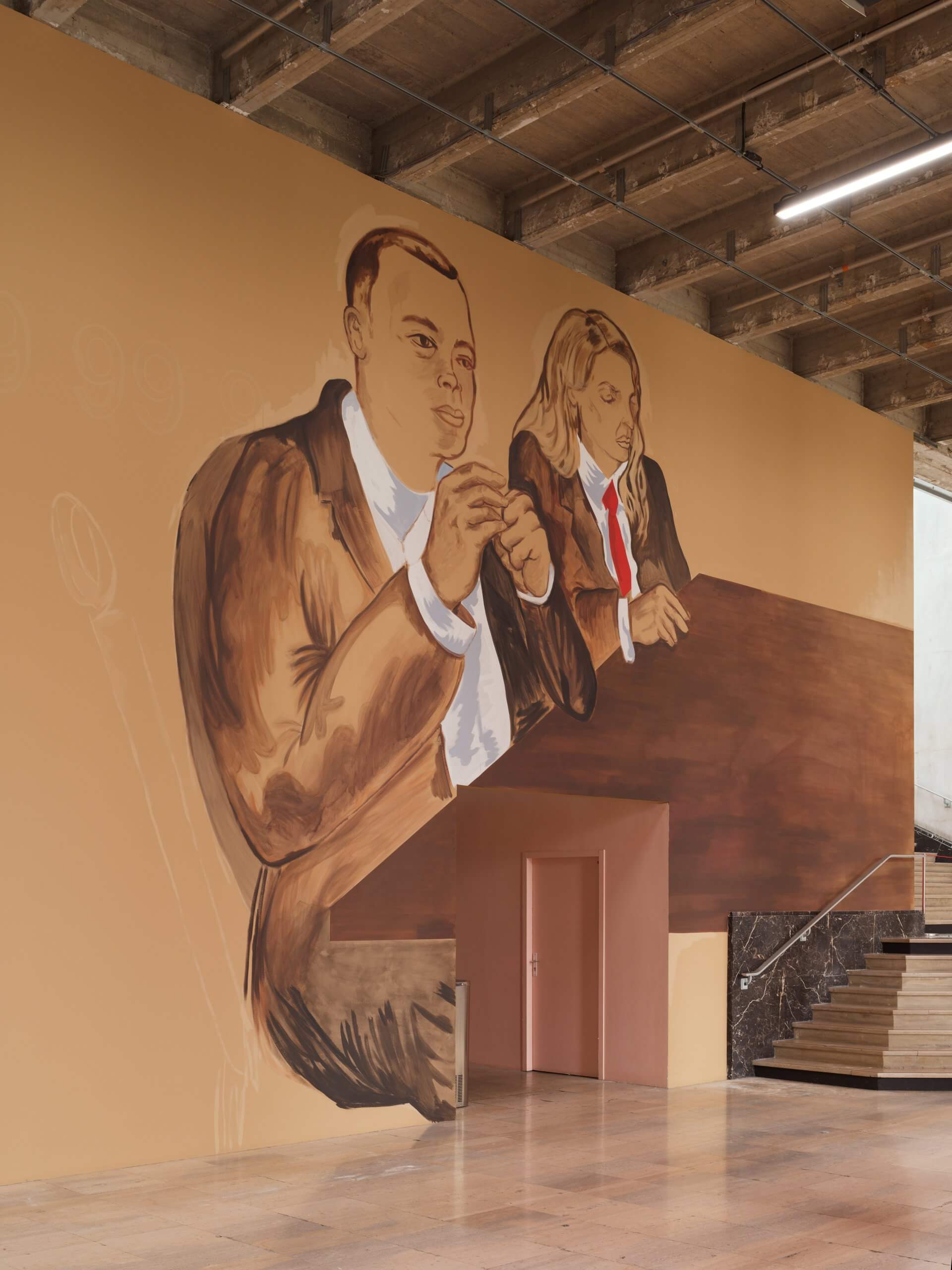 Une grande fresque représentant deux personnes en costume assises à une table est peinte sur un mur beige, au-dessus d'une porte, dans un intérieur de style industriel aux poutres en béton apparentes.