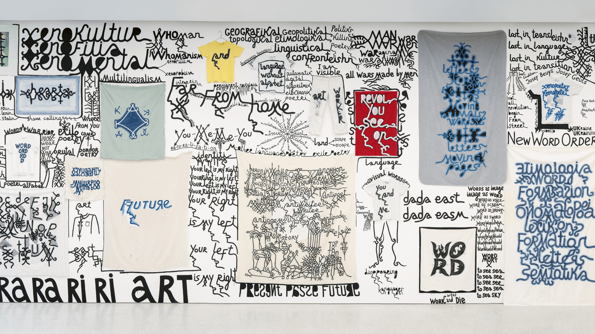 Un mur est orné de diverses affiches et t-shirts sur lesquels figurent des textes manuscrits, des dessins et des slogans en noir et bleu, avec des phrases sur l'art, la culture et l'avenir.
