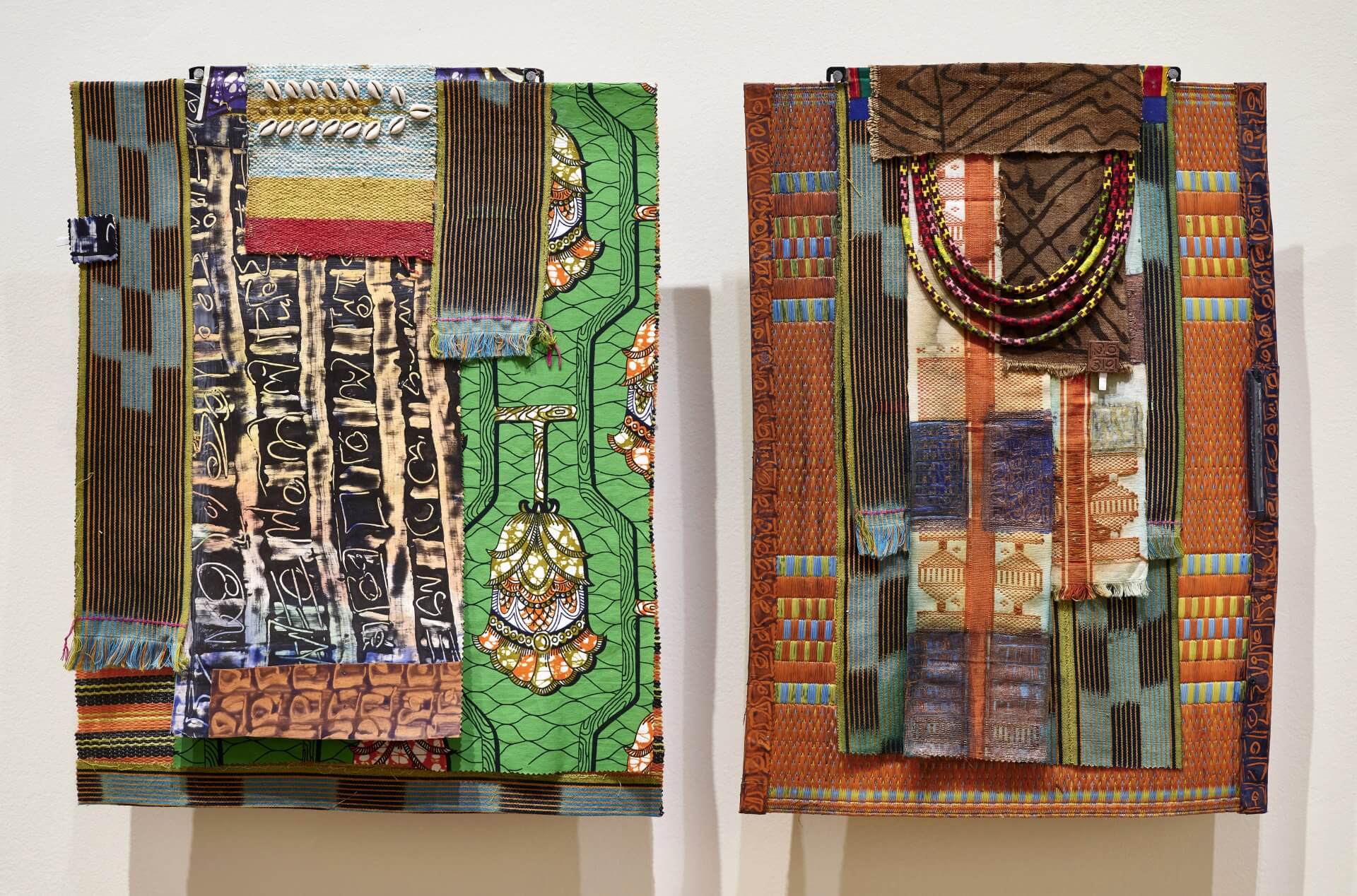 Deux œuvres d'art textile, composées de superpositions de tissus, de motifs audacieux et ornées de perles, sont exposées côte à côte sur un mur.