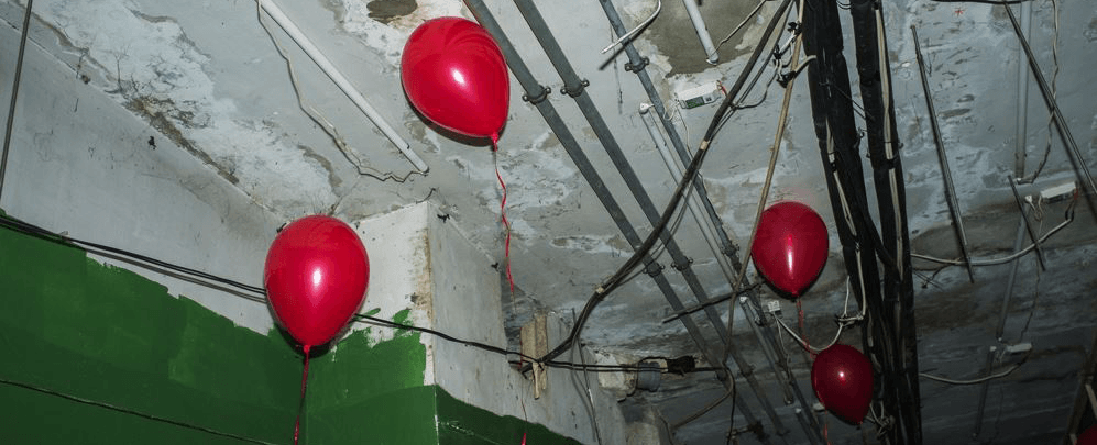 Quatre ballons rouges flottant devant un plafond où apparaissent des tuyaux et des câbles.